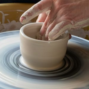 person making clay pot on white round plate